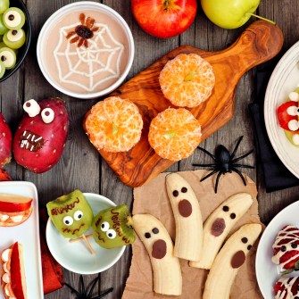 Healthy Halloween fruit snacks. Selection of fun, spooky treats. Top view table scene over a rustic wood background.