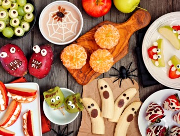 Healthy Halloween fruit snacks. Selection of fun, spooky treats. Top view table scene over a rustic wood background.