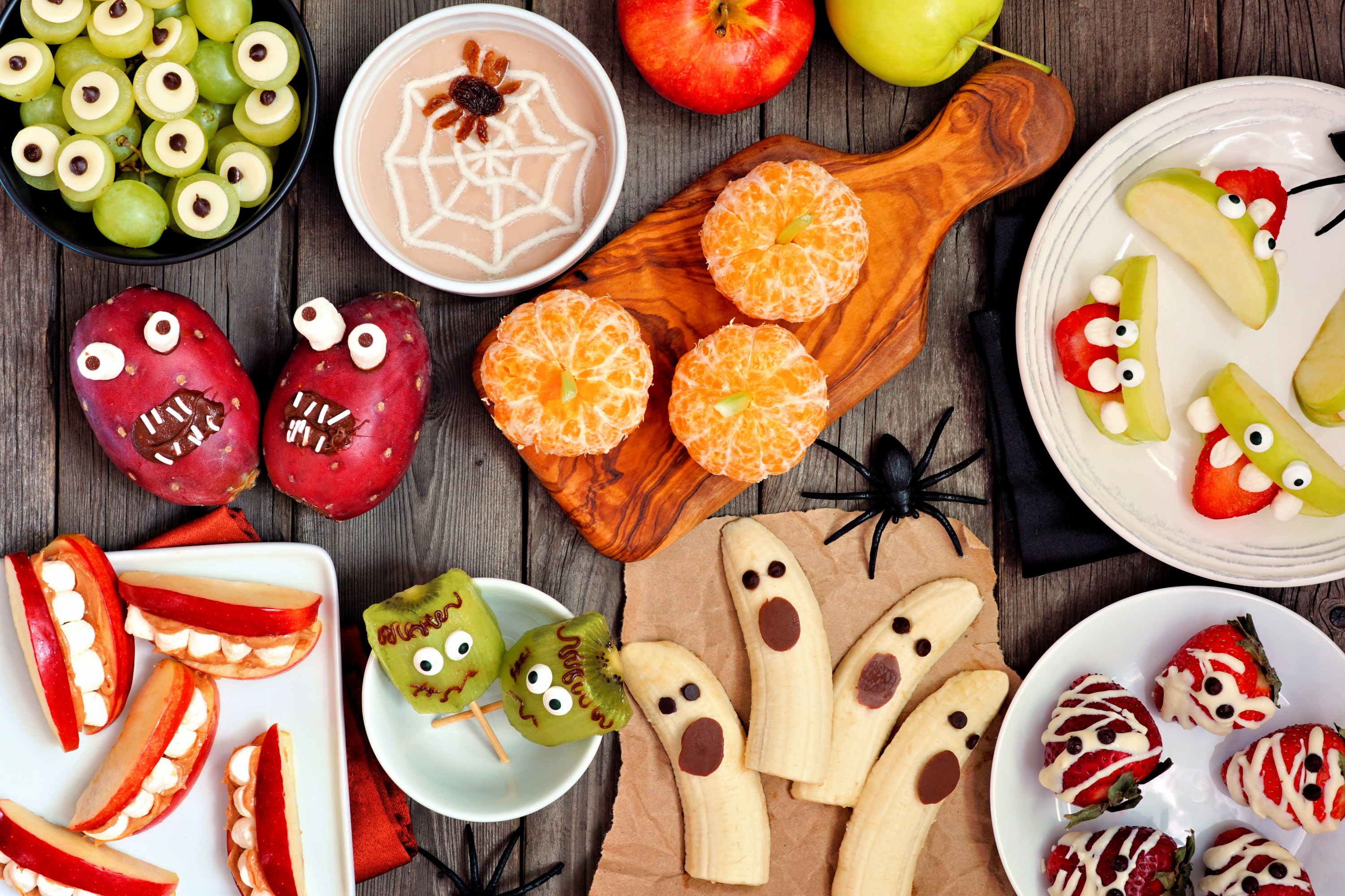 Healthy Halloween fruit snacks. Selection of fun, spooky treats. Top view table scene over a rustic wood background.