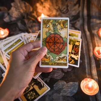 Hand holding tarot card with more tarot cards and candles in the background