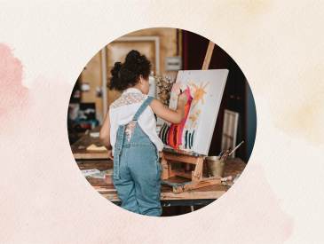 Young girl wearing overalls pains on a canvas.