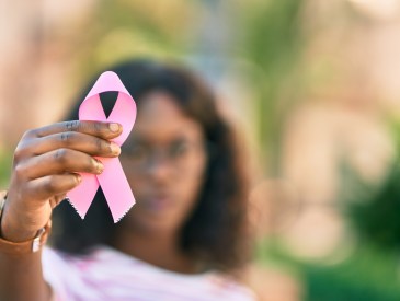 Young Black girl holding a pink breast cancer ribbon.