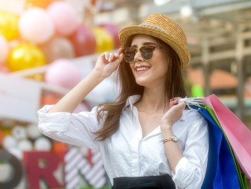 Happy young fashionable woman with shopping bags enjoying drinking coffee after shopping and holding take away coffee against urban background.