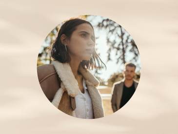 Woman with shoulder-length hair wearing tan sherpa jacket walks away from man in the distance.